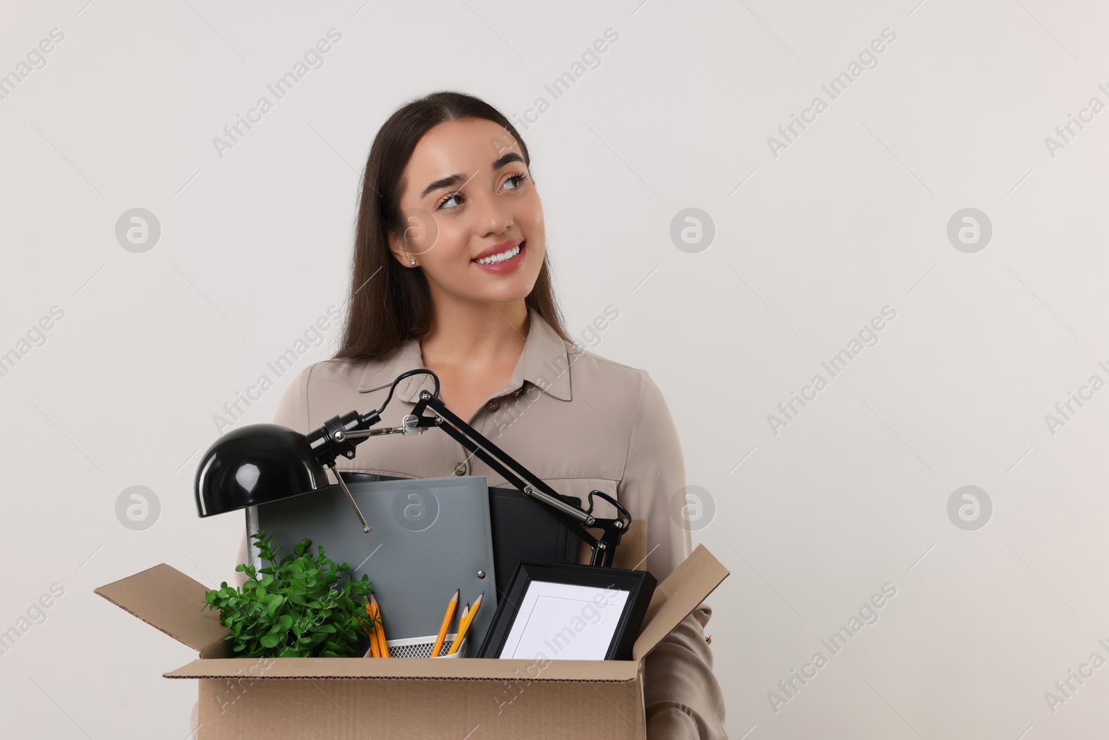 Photo of Happy unemployed woman with box of personal office belongings on white background, space for text