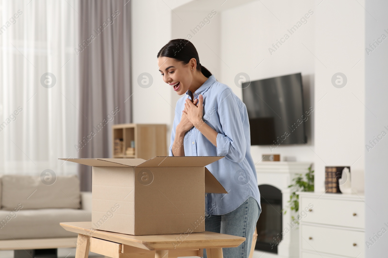 Photo of Emotional young woman with opened parcel at home. Internet shopping