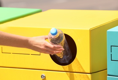 Woman throwing plastic bottle into sorting bin on city street, closeup. Recycling waste