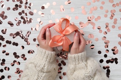Photo of Christmas present. Woman with gift box and confetti on white wooden background, top view