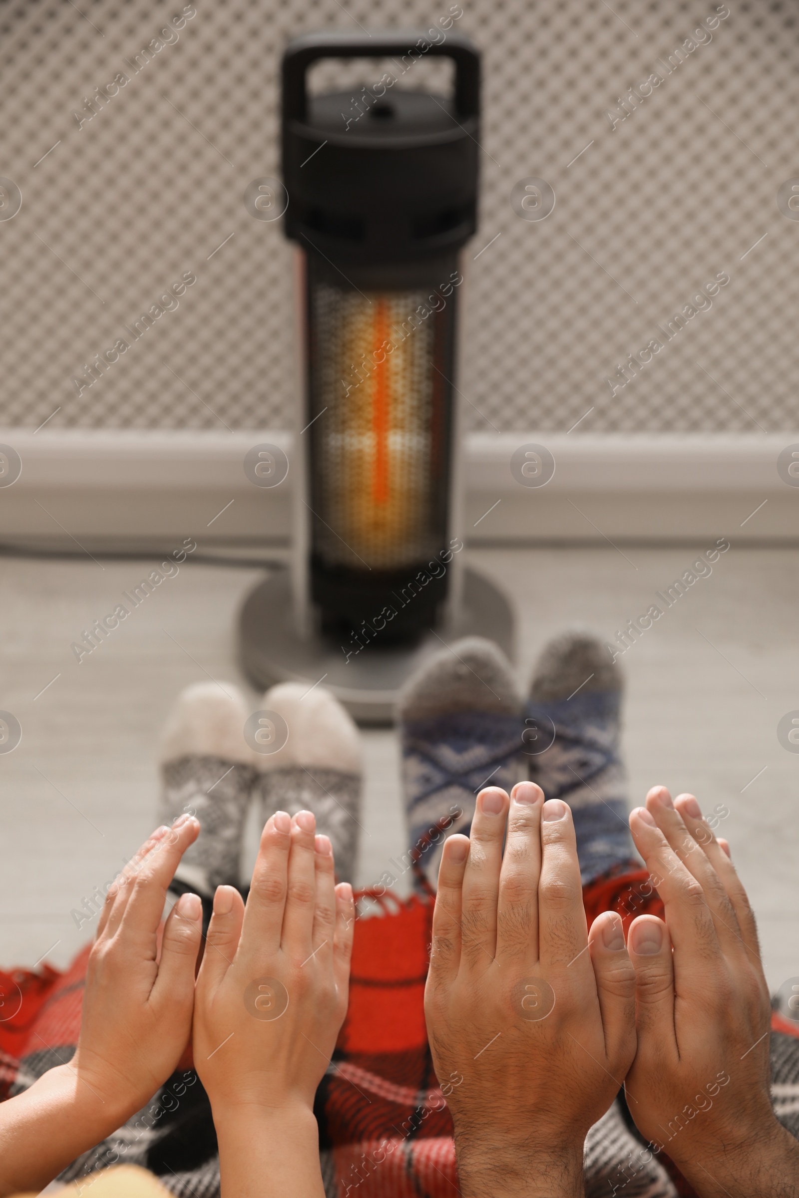 Photo of Couple warming feet and hands near modern heater indoors, closeup