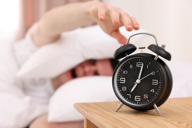 Photo of Yawning man turning off alarm clock in bedroom, focus on hand. Space for text