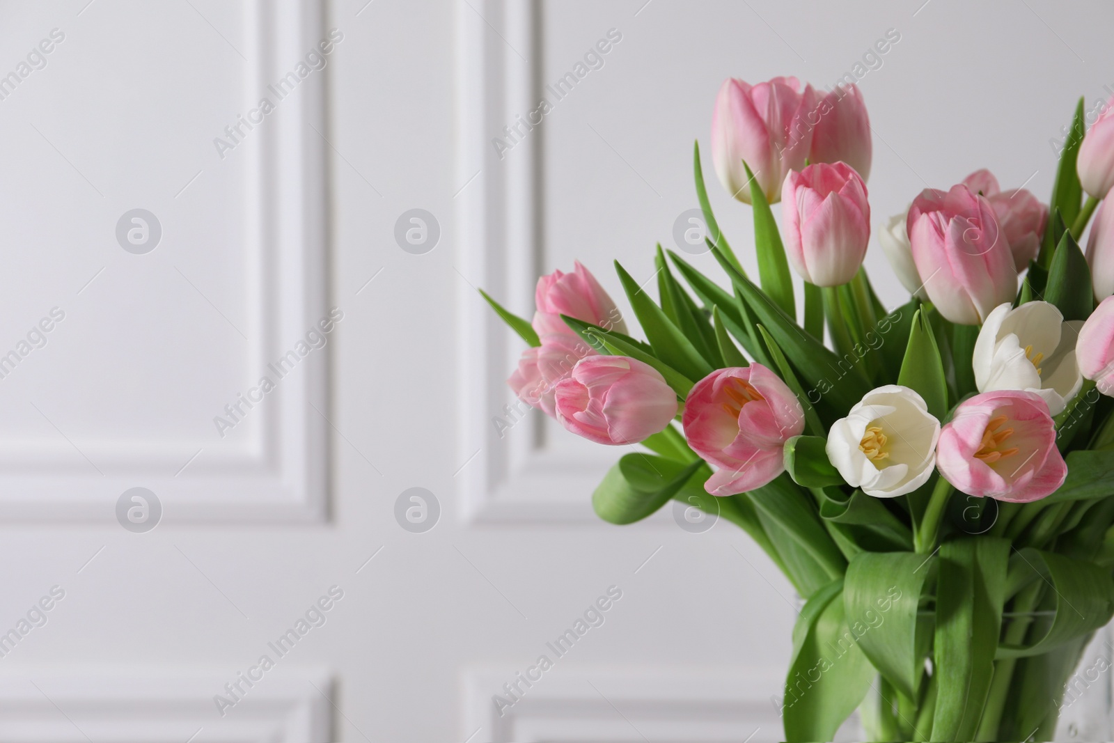 Photo of Beautiful bouquet of tulips in glass vase against white wall. Space for text