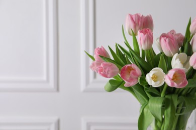 Photo of Beautiful bouquet of tulips in glass vase against white wall. Space for text