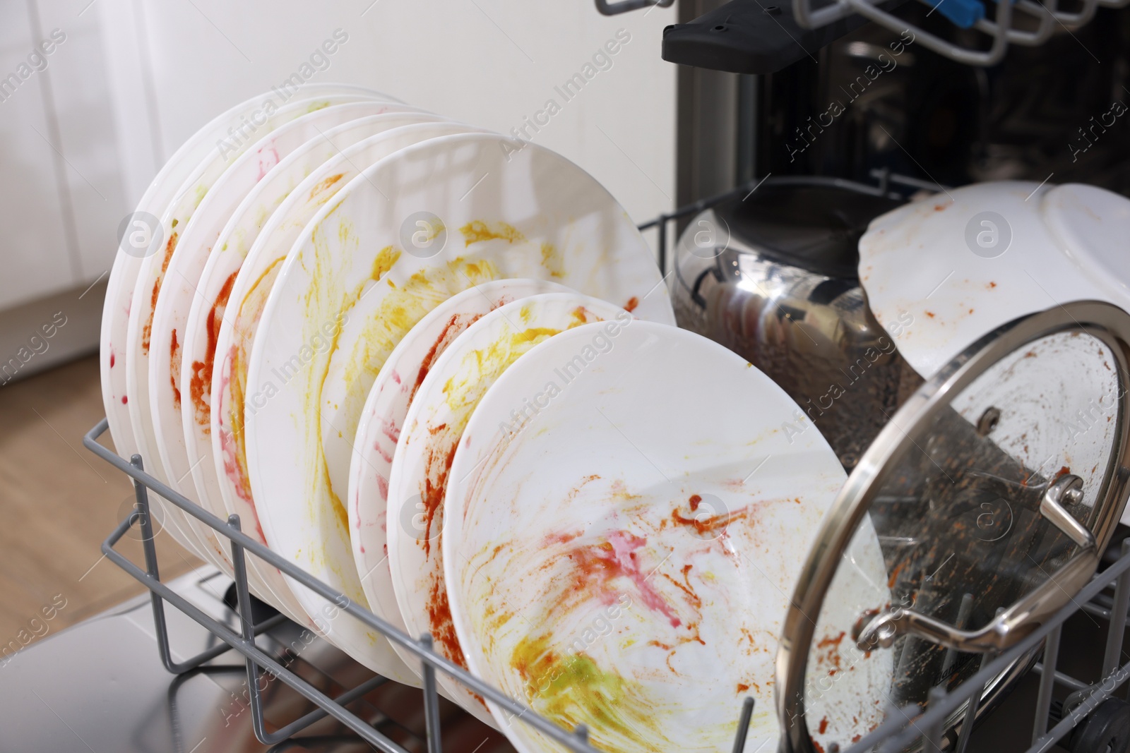 Photo of Open modern dishwasher with dirty tableware in kitchen, closeup