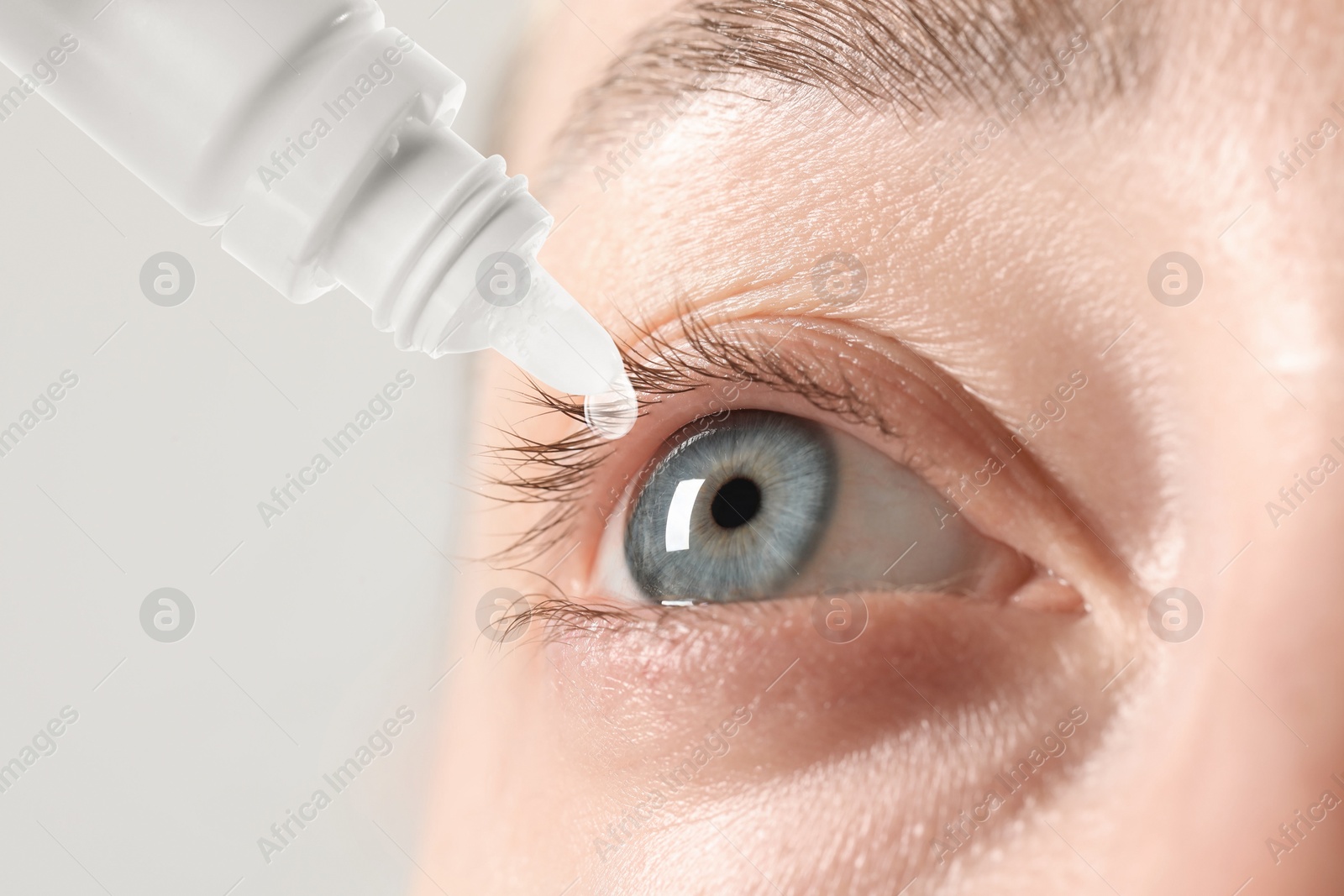 Image of Woman applying eye drops on light background, closeup