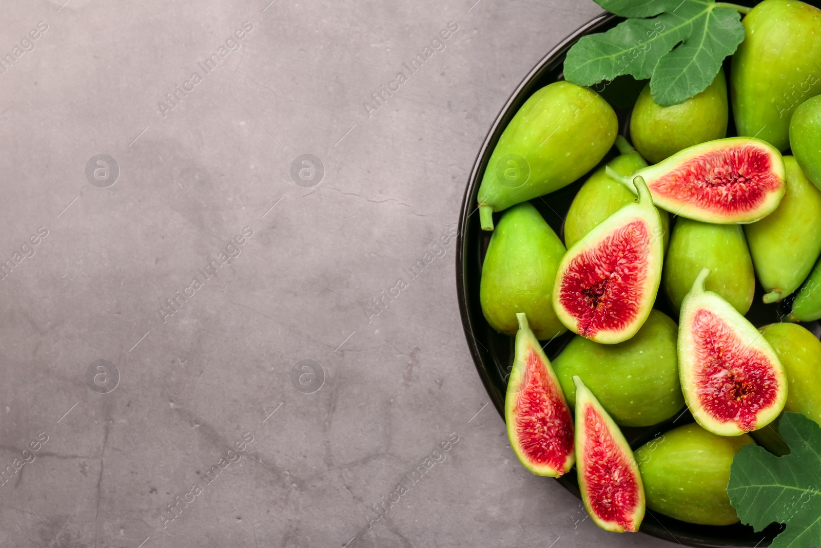 Photo of Cut and whole green figs on light gray table, top view. Space for text