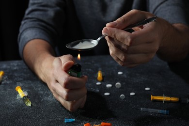 Man preparing drugs with spoon and lighter at black textured table, closeup