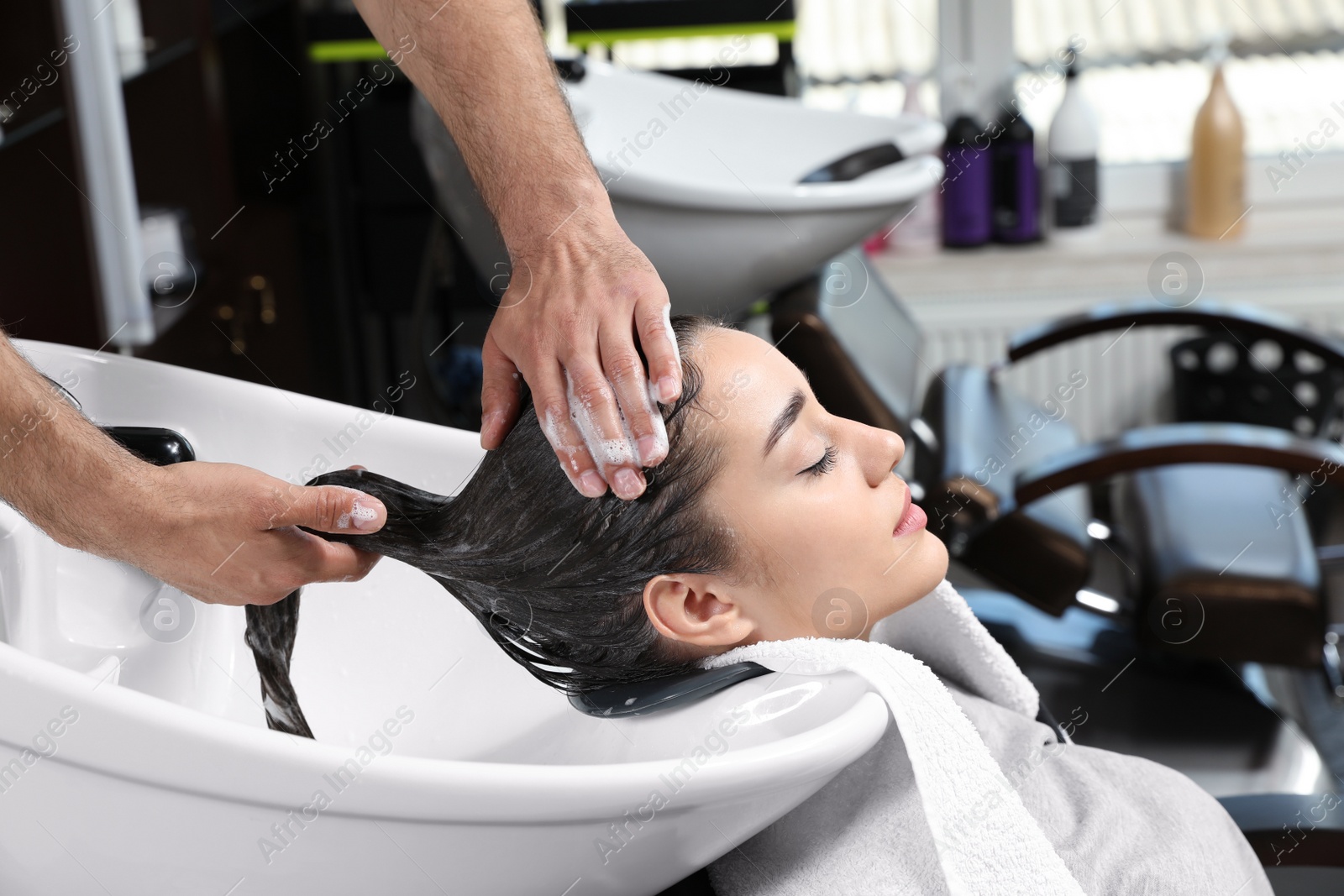 Photo of Stylist washing client's hair at sink in beauty salon