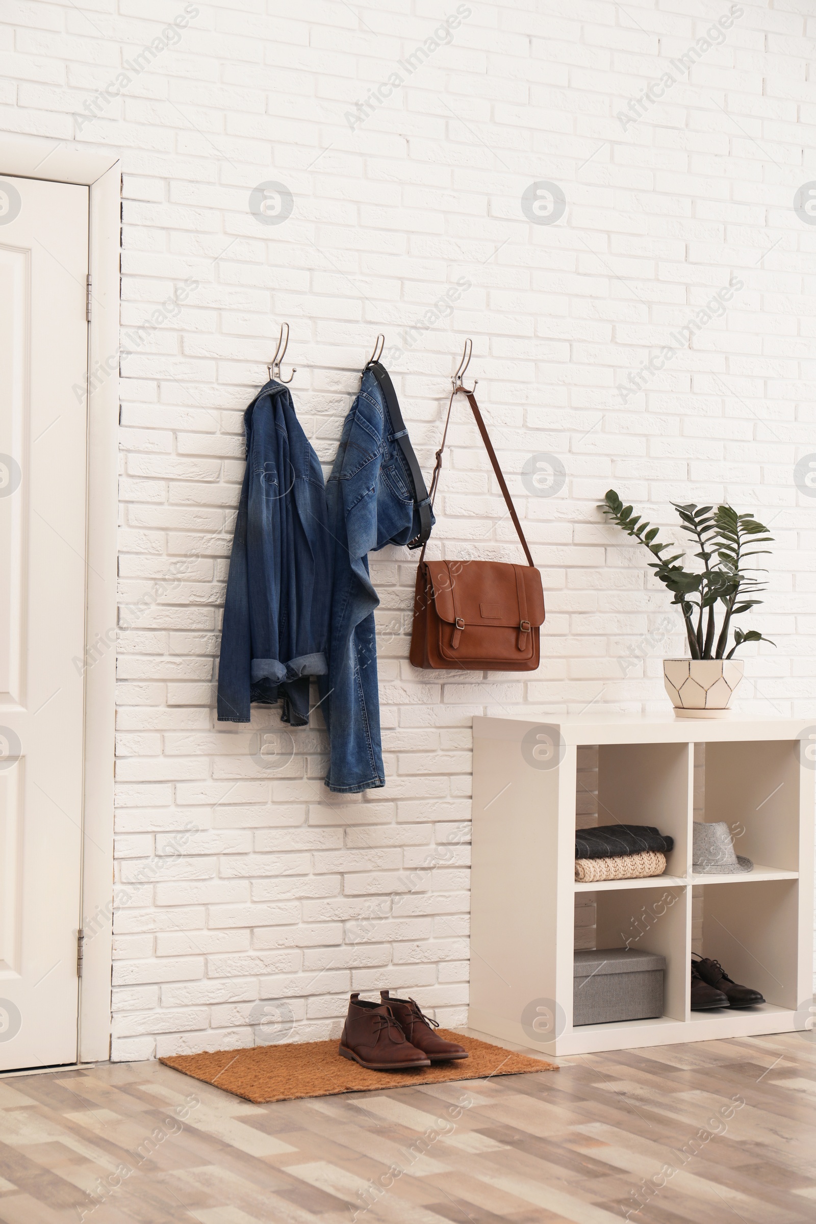 Photo of Stylish hallway interior with comfortable furniture and clothes on brick wall