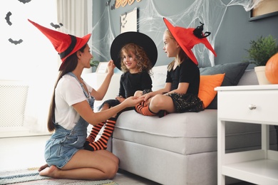 Photo of Mother and cute little girls wearing Halloween costumes at home