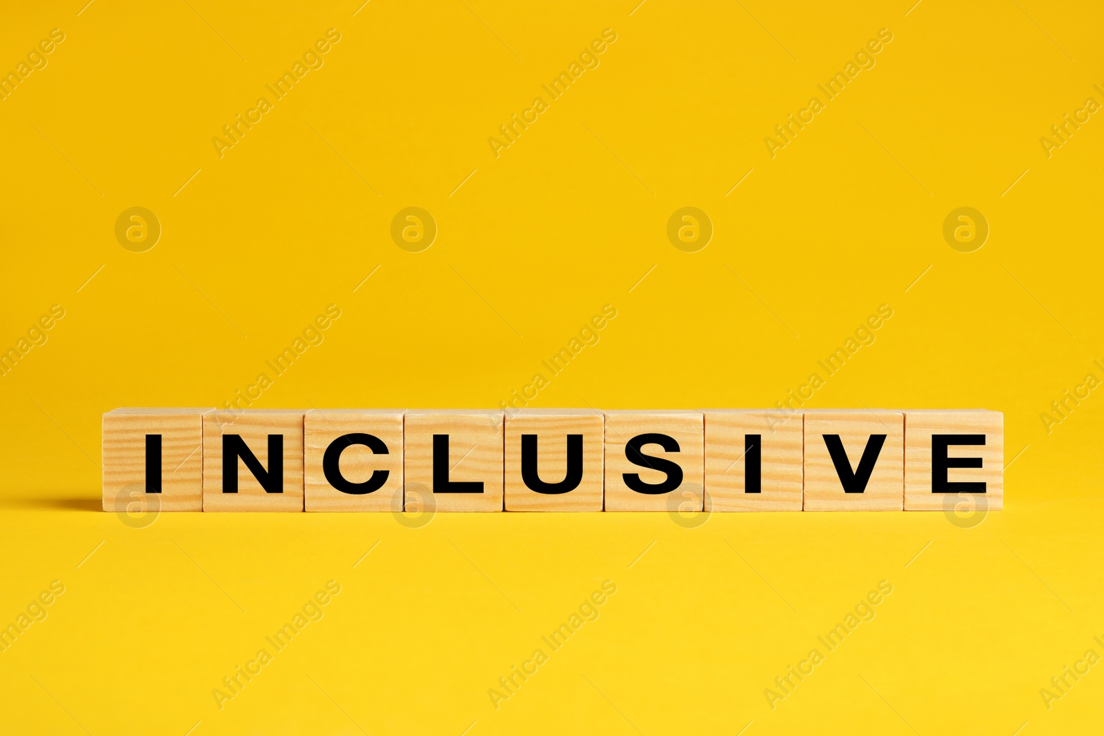 Photo of Wooden cubes with word Inclusive on yellow background. Space for text