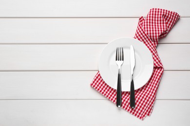 Ceramic plate, fork and knife on white wooden table, top view