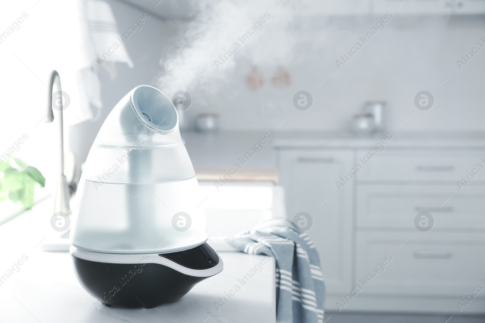 Photo of Modern air humidifier on counter in kitchen. Space for text