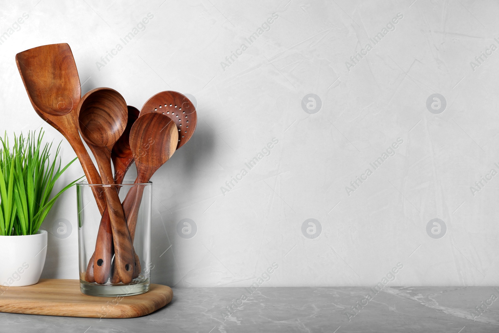 Photo of Set of wooden kitchen utensils in glass holder and houseplant on light grey marble table. Space for text