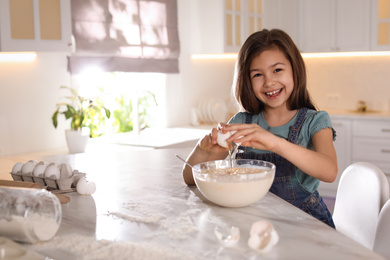 Cute little girl cooking dough in kitchen at home
