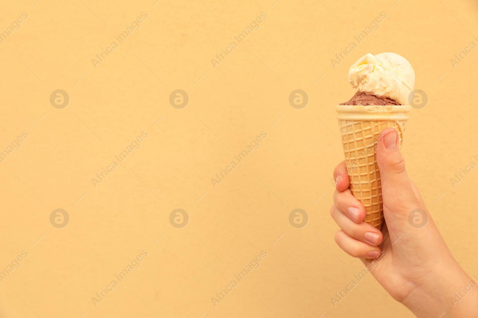 Photo of Woman holding waffle cone with delicious ice cream against yellow wall, closeup. Space for text