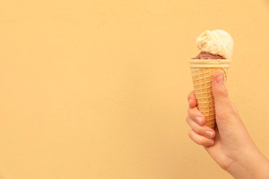 Woman holding waffle cone with delicious ice cream against yellow wall, closeup. Space for text