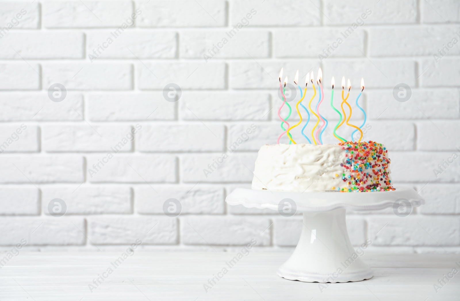 Photo of Birthday cake with candles on table against brick wall