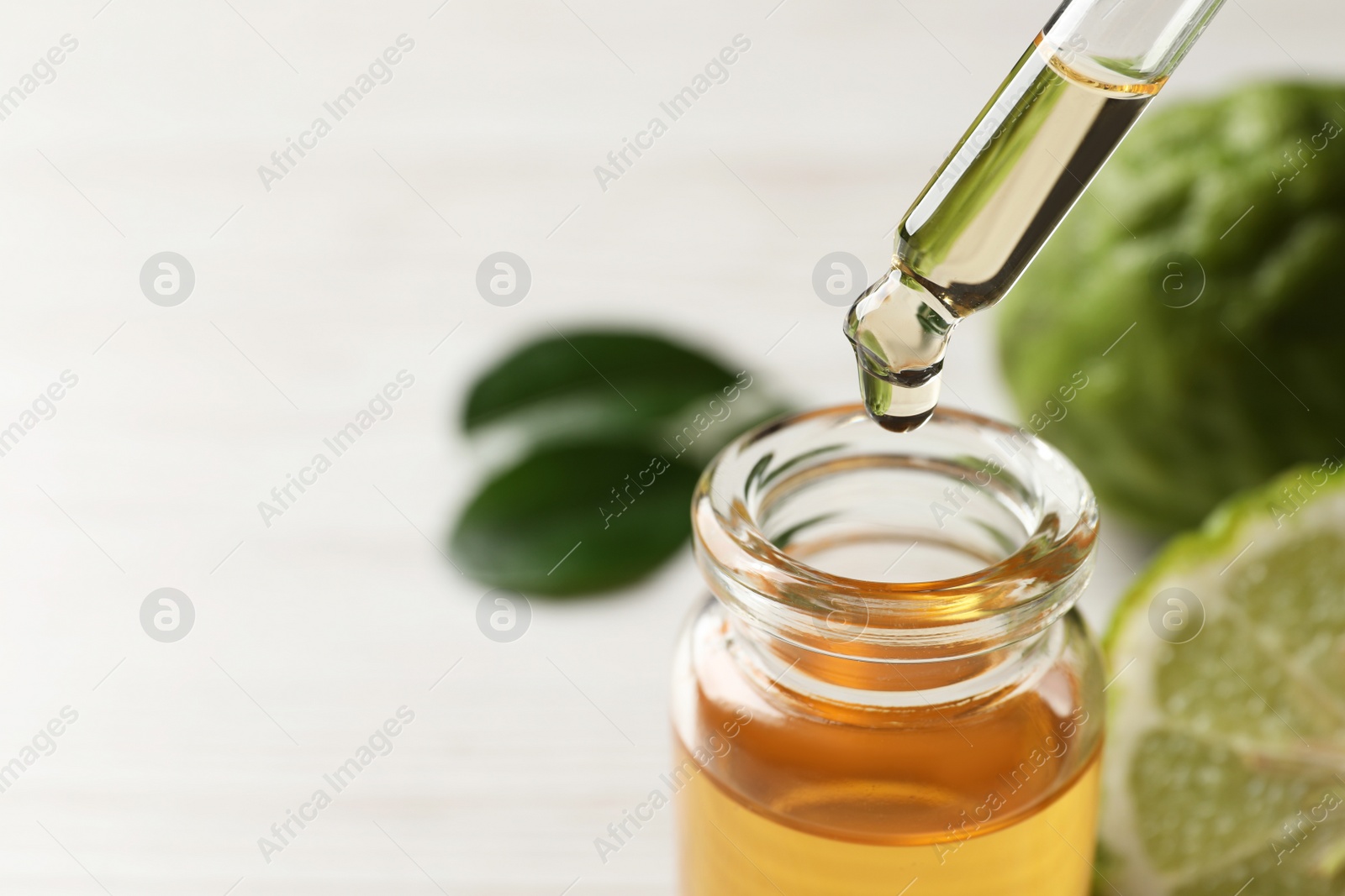 Photo of Dripping bergamot essential oil into glass bottle on table, closeup. Space for text