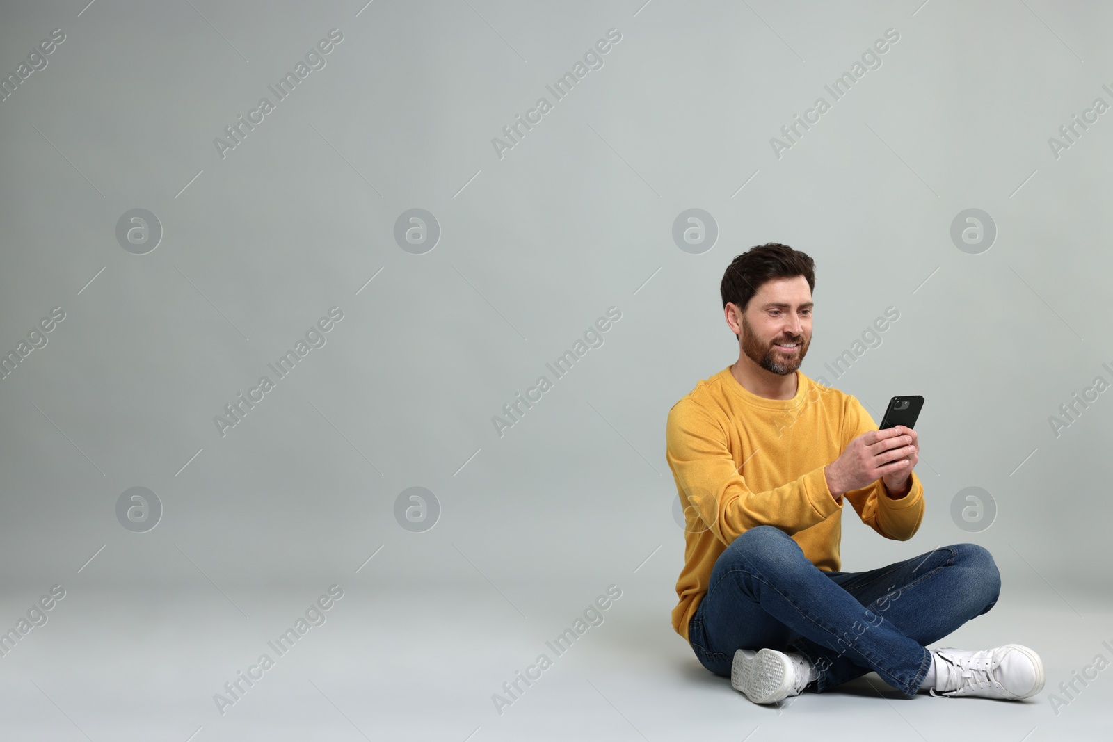 Photo of Smiling man with smartphone on grey background. Space for text