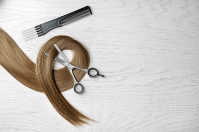 Photo of Flat lay composition with hair lock and tools on wooden background. Space for text