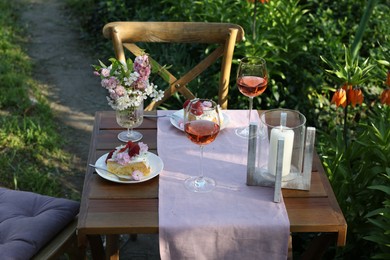 Vase with spring flowers, wine and cake on table served for romantic date in garden