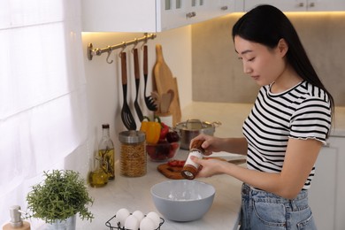 Photo of Cooking process. Beautiful woman adding salt into bowl in kitchen