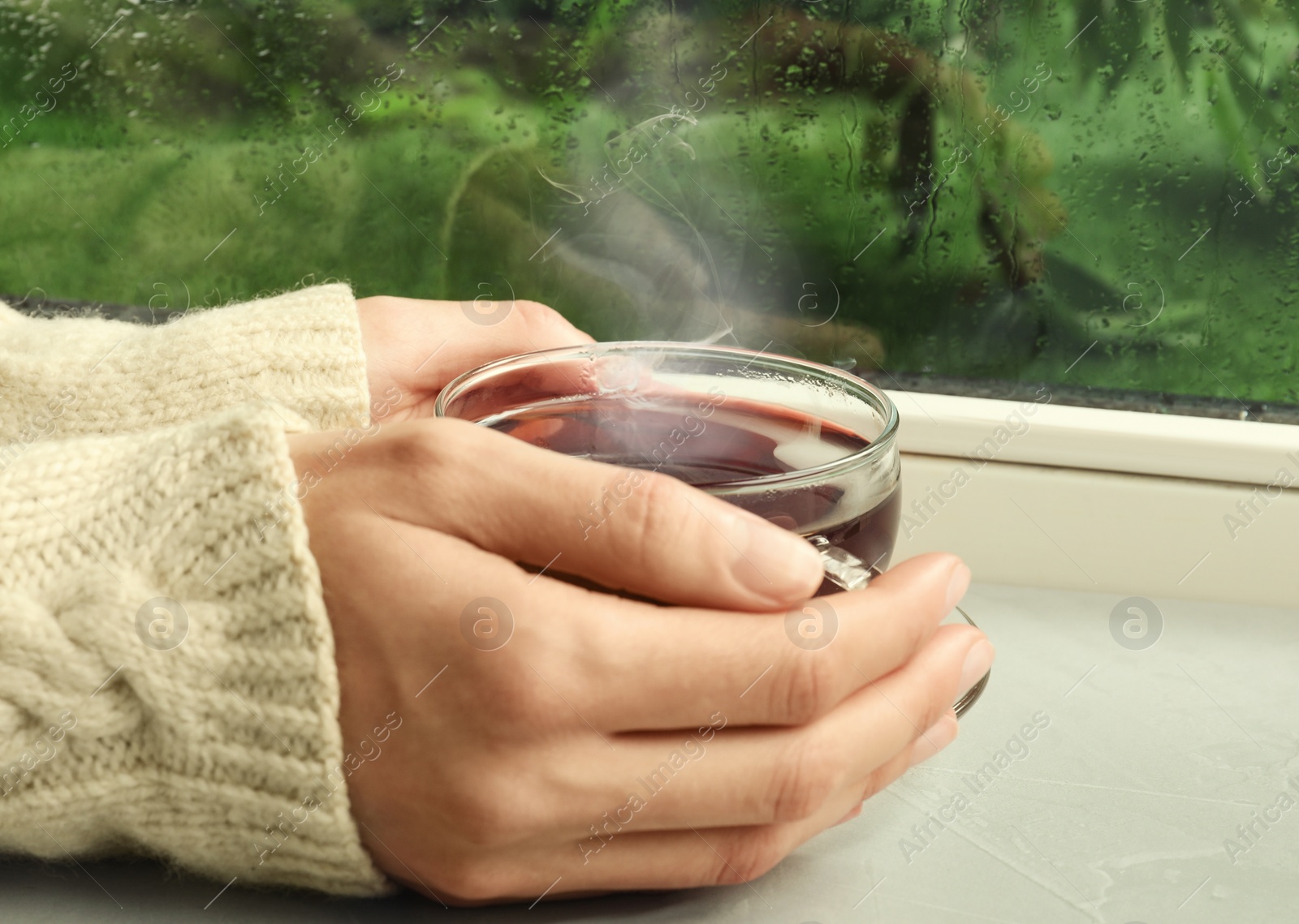 Image of Woman with cup of hot drink near window on rainy day, closeup