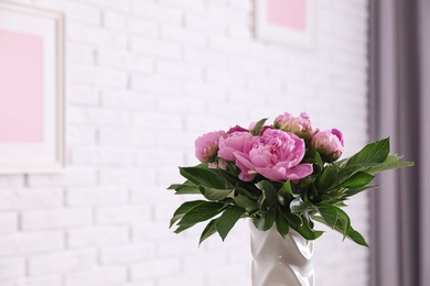 Photo of Vase with bouquet of beautiful peonies at white wall in room, space for text