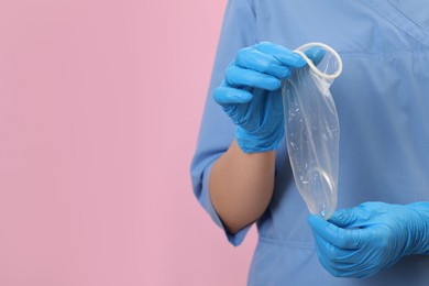 Photo of Doctor with unrolled female condom on pink background, closeup. Space for text
