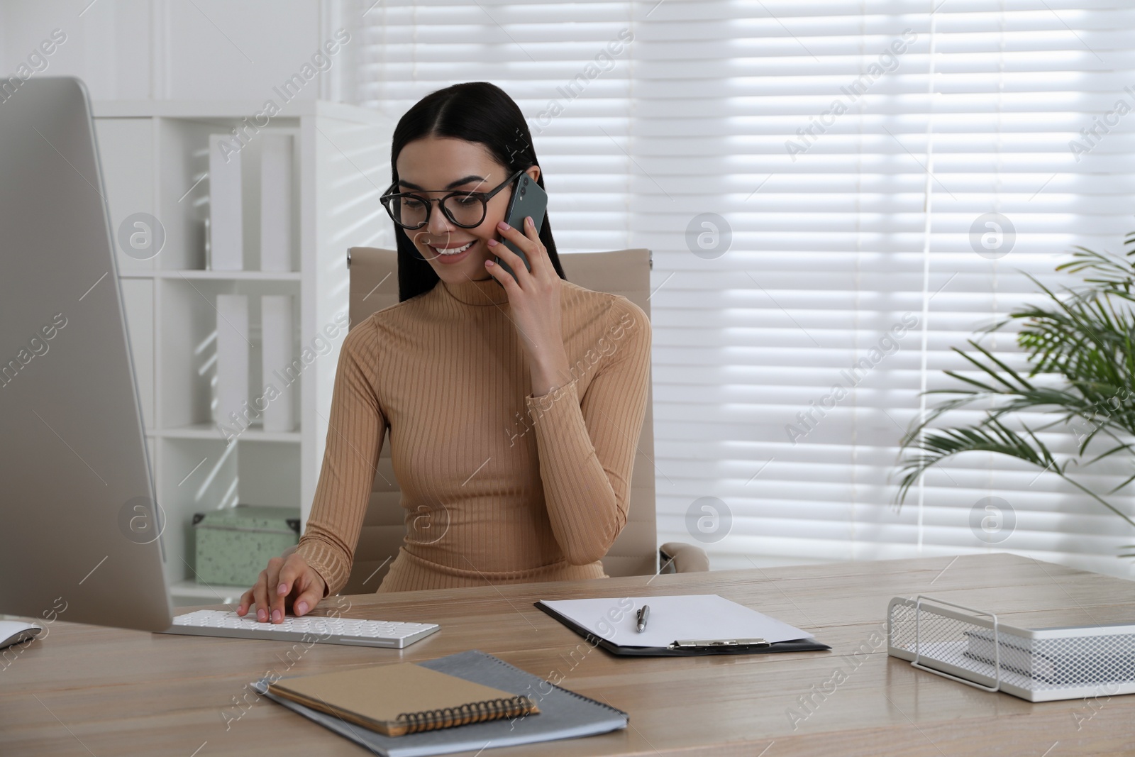 Photo of Secretary talking on smartphone at wooden table in office