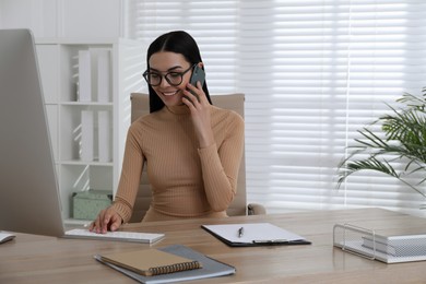 Secretary talking on smartphone at wooden table in office