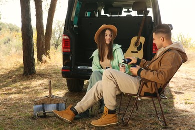 Couple resting in camping chairs and enjoying hot drink outdoors