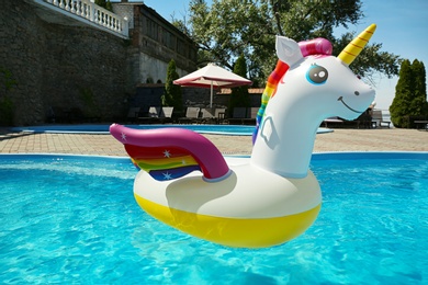 Photo of Funny inflatable unicorn ring floating in swimming pool on sunny day, outdoors