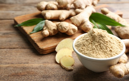 Photo of Dry ginger powder, fresh root and leaves on wooden table. Space for text