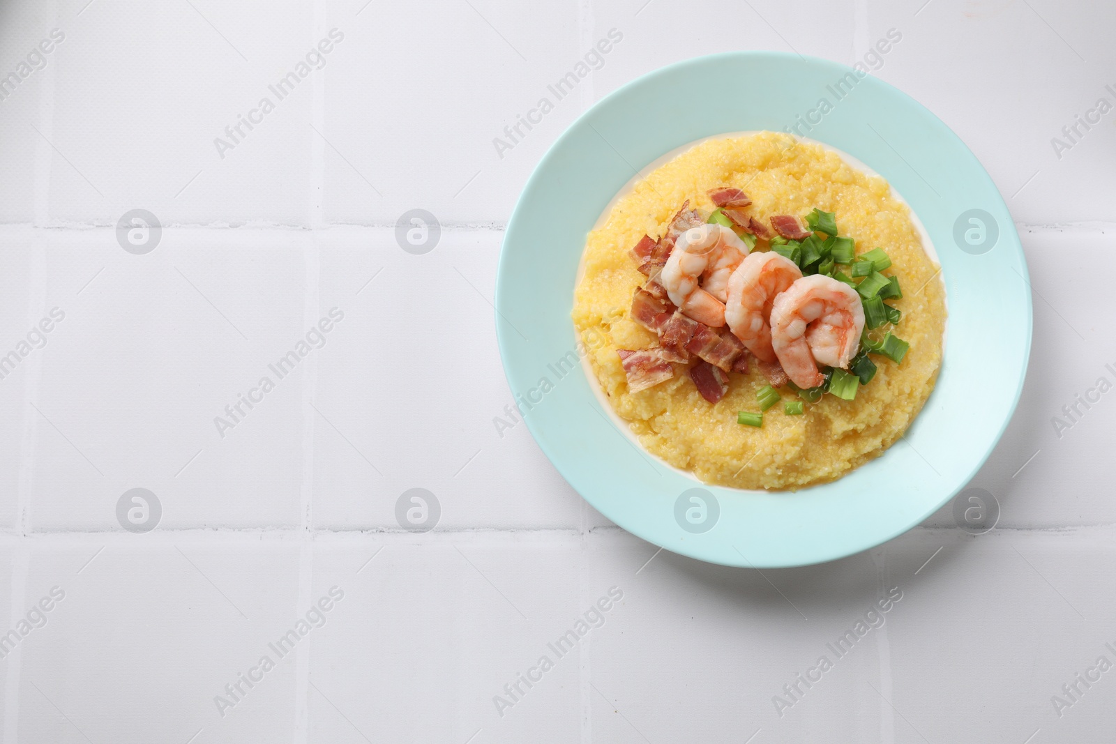 Photo of Plate with fresh tasty shrimps, bacon, grits and green onion on white tiled table, top view. Space for text