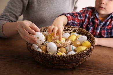 Little boy and his mother with basket full of dyed Easter eggs at wooden table, closeup. Easter celebration