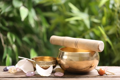 Photo of Composition with tibetan singing bowl and different gemstones on wooden table outdoors. Sound healing