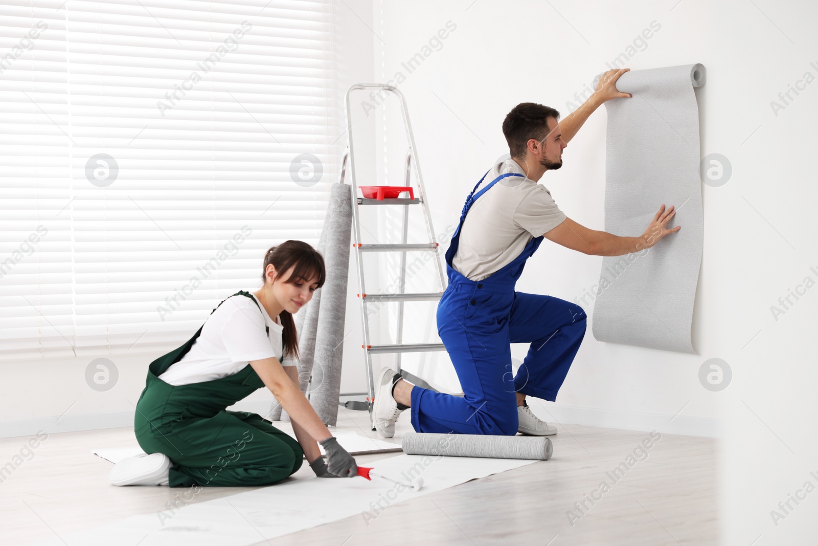 Photo of Woman applying glue onto wallpaper while man hanging sheet indoors