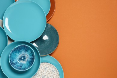 Photo of Different plates and bowl on orange background, flat lay. Space for text
