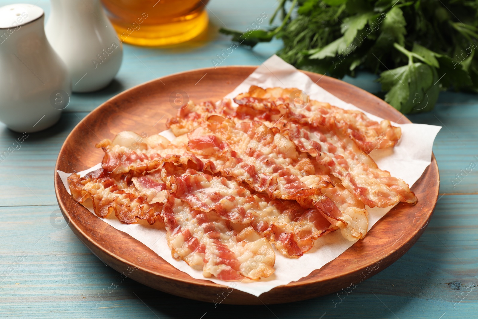 Photo of Delicious fried bacon slices on blue wooden table, closeup