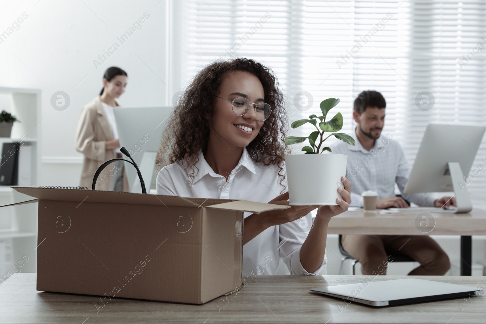 Photo of New coworker unpacking box with personal items at workplace in office