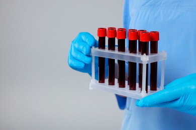 Laboratory testing. Doctor with blood samples in tubes on light grey background, closeup. Space for text