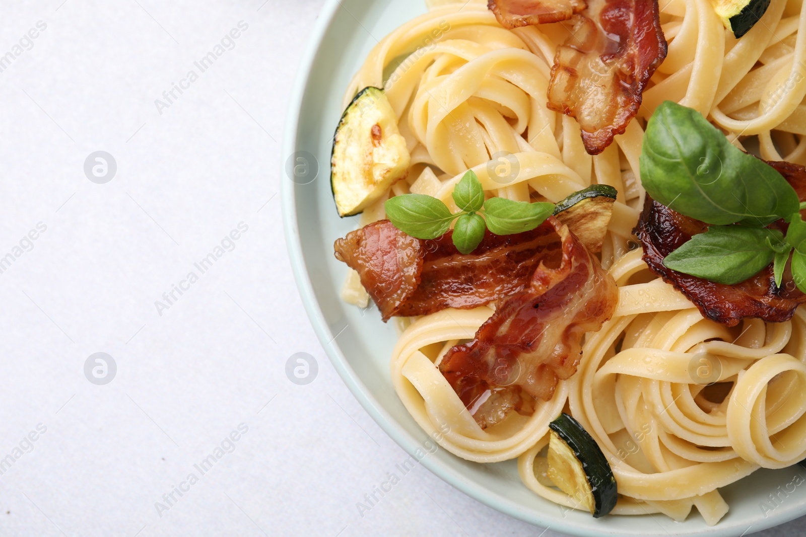 Photo of Tasty pasta with bacon and basil on light grey table, top view. Space for text