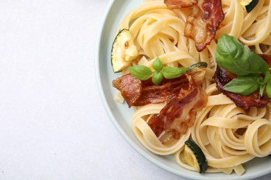 Tasty pasta with bacon and basil on light grey table, top view. Space for text