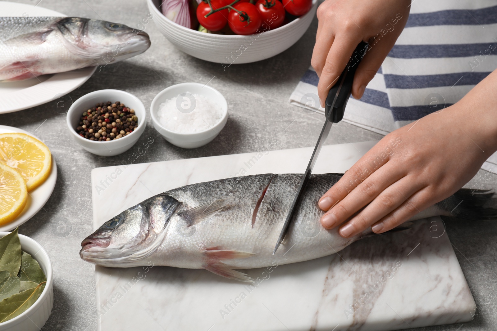 Photo of Woman cutting fresh raw sea bass fish at light gray table, closeup