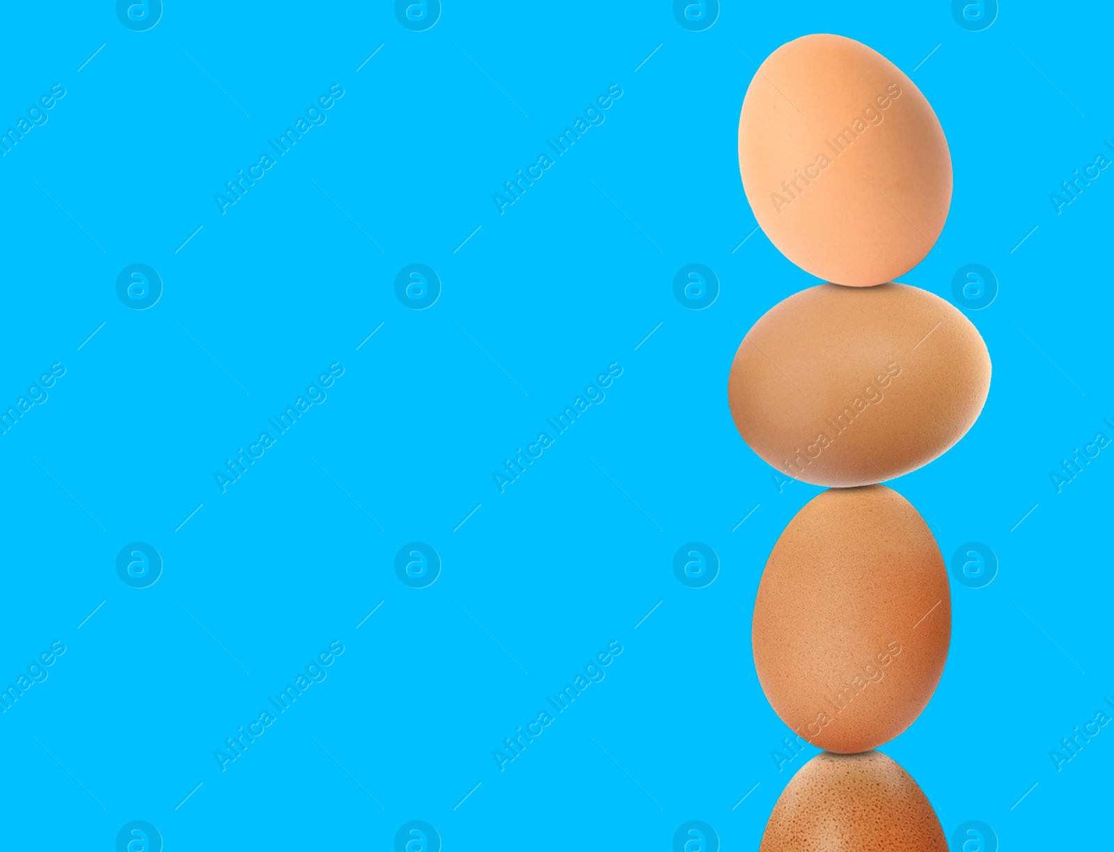 Image of Stacked fresh chicken eggs against light blue background. Space for text