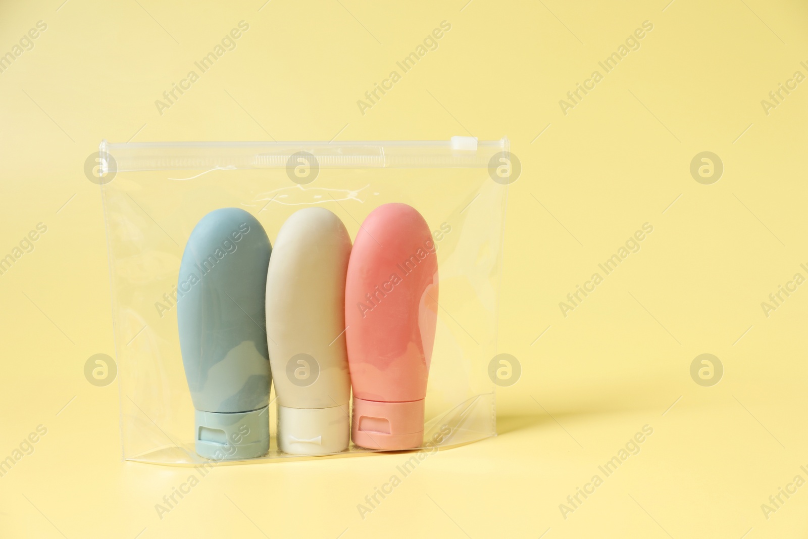 Photo of Cosmetic travel kit in plastic bag on yellow background, space for text