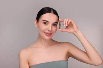 Beautiful young woman holding skincare ampoule on grey background